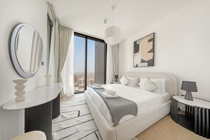 Ein modernes Hotelzimmer mit einem großen Bett, einem runden Spiegel, einem Nachttisch mit Lampe und Blick auf die Stadt durch ein großes Fenster.