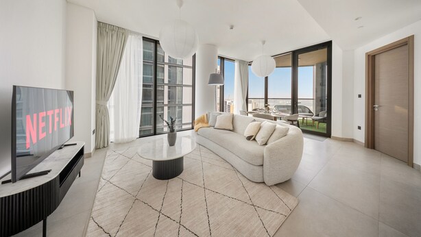 A modern living room with a large flat-screen TV, a white sofa, and a coffee table. - Stylish 2BR + Maid’s Apartment in Sobha Hartland (Dubai)