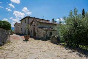 A stone building with a courtyard, a large potted plant, and a rustic fence. - Holiday Home 'Capriata' with Shared Pool, Wi-Fi and Air Conditioning (Bagno a Ripoli)