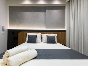 A hotel room with a bed, two pillows, a headboard, a phone, and a curtain. - Solaz by Hosppedar (João Pessoa)