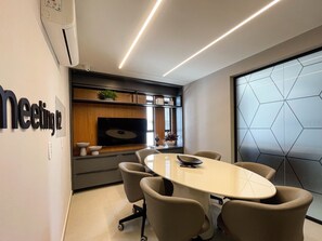 A conference room with a round table, six chairs, a flat-screen TV, and a wall-mounted shelf with decorative items. - Solaz by Hosppedar (João Pessoa)