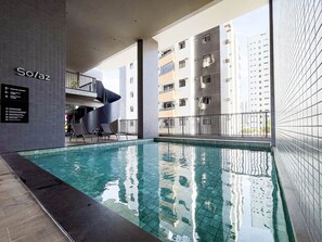An indoor swimming pool with a modern design, a sign indicating 'Solaz Smart Living,' and a view of surrounding high-rise buildings. - Solaz by Hosppedar (João Pessoa)