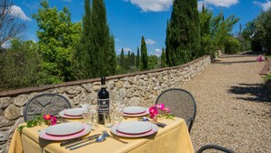 Ein Tisch im Freien mit einer Steinmauer im Hintergrund, einer Flasche Chianti-Wein und rosa Blumen.