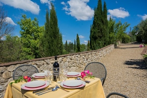 A table set outdoors with a stone wall backdrop, a bottle of Chianti wine, and pink flowers. - Holiday Home 'Romantica' with Shared Pool, Wi-Fi and Air Conditioning (Bagno a Ripoli)