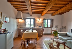 A kitchen with wooden beams, a dining table, chairs, a sofa, and a potted plant. - Holiday Home 'Romantica' with Shared Pool, Wi-Fi and Air Conditioning (Bagno a Ripoli)