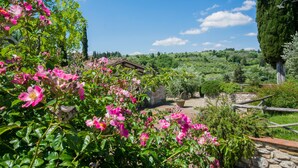 Ein Garten mit blühenden rosa Blumen, einer Steinmauer und einem rustikalen Gebäude.