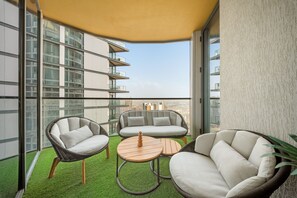 A balcony with wicker furniture, a round wooden table, and a view of a cityscape. - Sobha Hartland Waves Grande -2805 2BD (Dubai)
