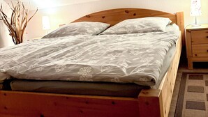 Een houten bed met een bloemenbed overdekt in een kamer met witte muren en een houten vloer.