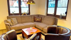 Een woonkamer met een hoekbank, twee leren fauteuils, een houten salontafel en een hanglamp.