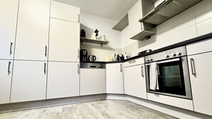 Een moderne keuken met witte kastjes, een inbouwoven en een koffiezetapparaat op het aanrecht.