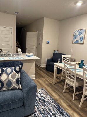 Ein modernes Wohnzimmer mit einem blauen Sofa, einem Essbereich mit weißen Stühlen und einer Küche mit einer weißen Kochinsel.