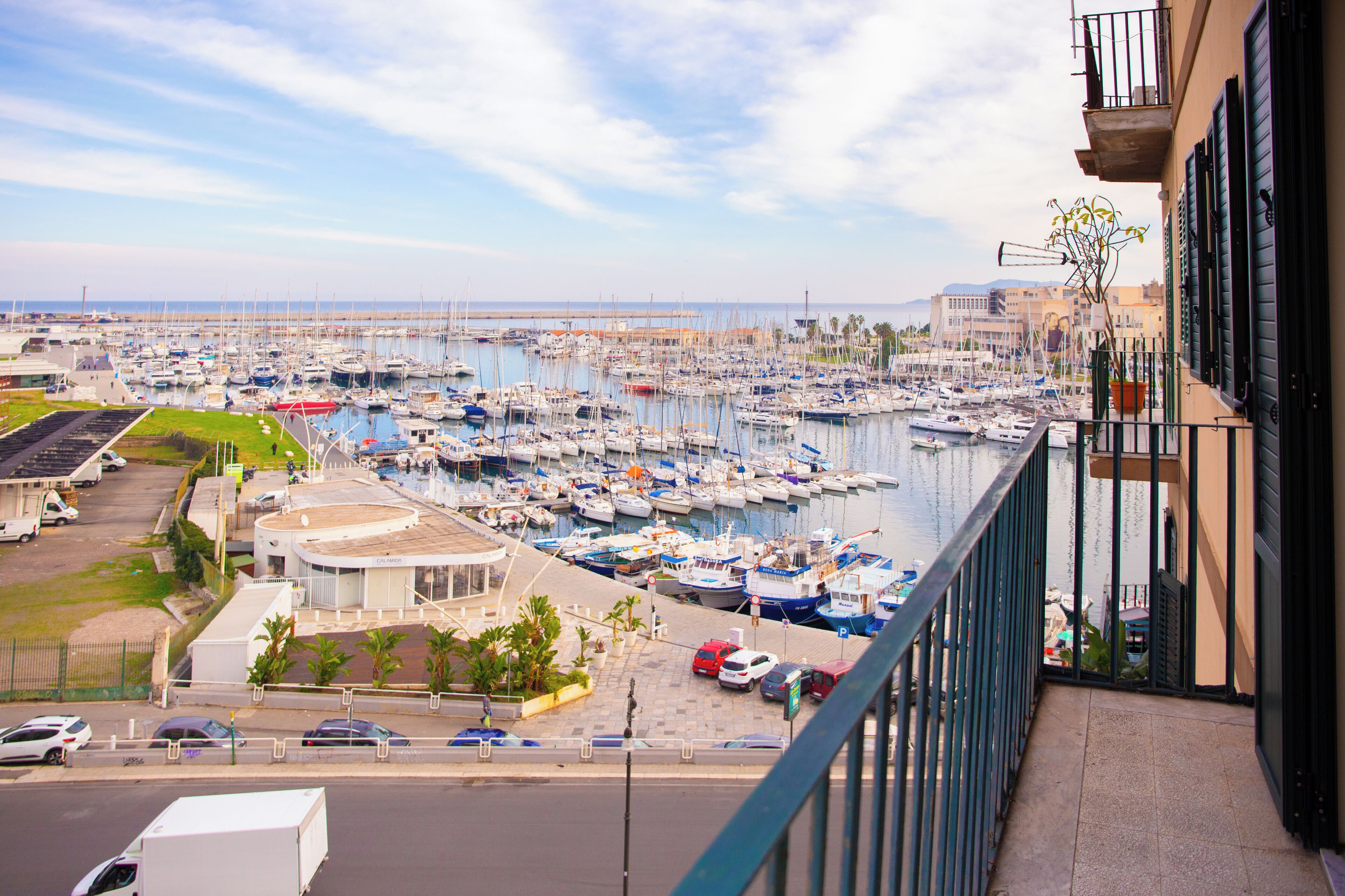 A marina with numerous boats docked, a parking area with cars, and a building with a balcony overlooking the marina.
