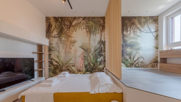 Ein modernes Schlafzimmer mit einem großen Bett, einem Fernseher und einem Wandgemälde im tropischen Stil.