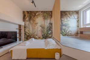 Un dormitorio moderno con una cama grande, un televisor y un mural tropical en la pared.