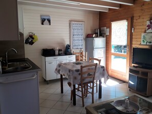 A compact kitchen with a sink, stove, and refrigerator. There is a dining table with chairs and a television on a stand. - Charming Small Holiday Home with Private Terrace, Garden, and Air Conditioning (La Teste-de-Buch)