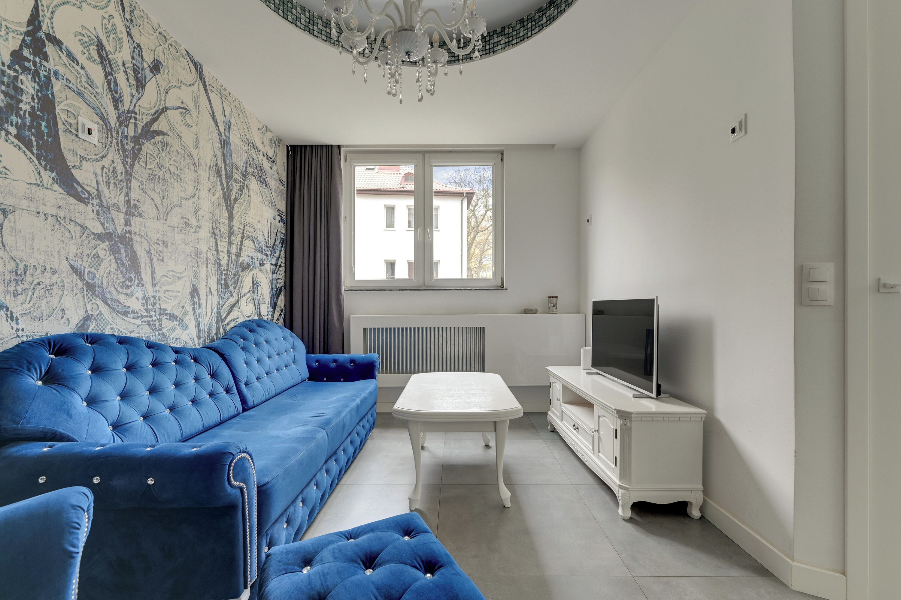 A living room with a blue sofa, a white coffee table, and a TV on a white cabinet.