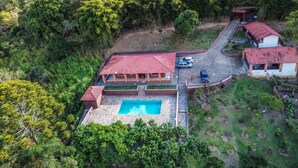 An aerial view of a house with a swimming pool, surrounded by dense greenery and hills. - Chácara Paraíso de Itamonte (Itanhandu)