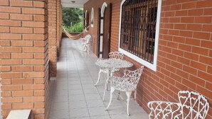 A covered corridor with brick walls, white metal chairs, and a tiled floor. - Chácara Paraíso de Itamonte (Itanhandu)