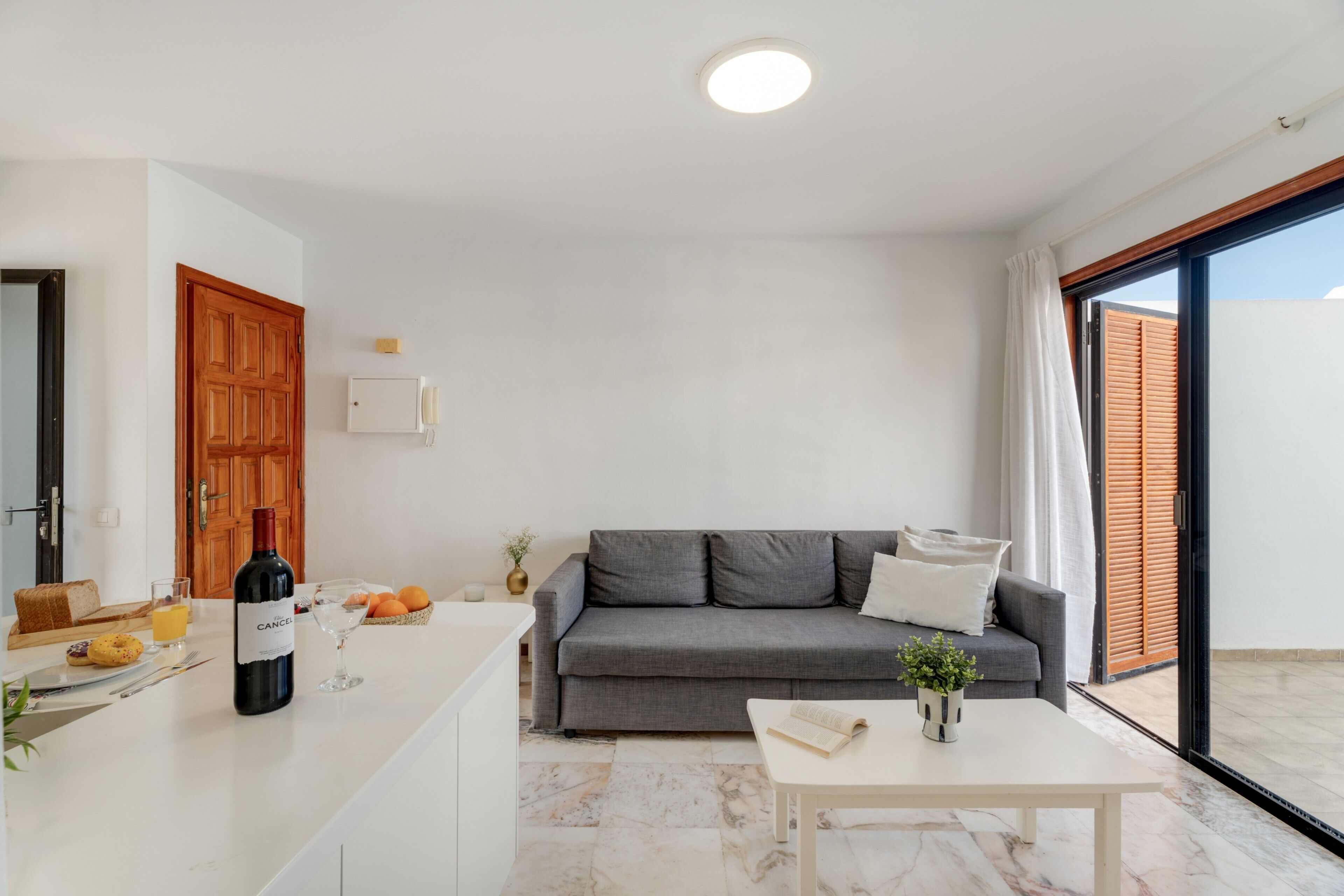 A modern living room with a grey sofa, a white coffee table, and a dining area with a wooden table and chairs.