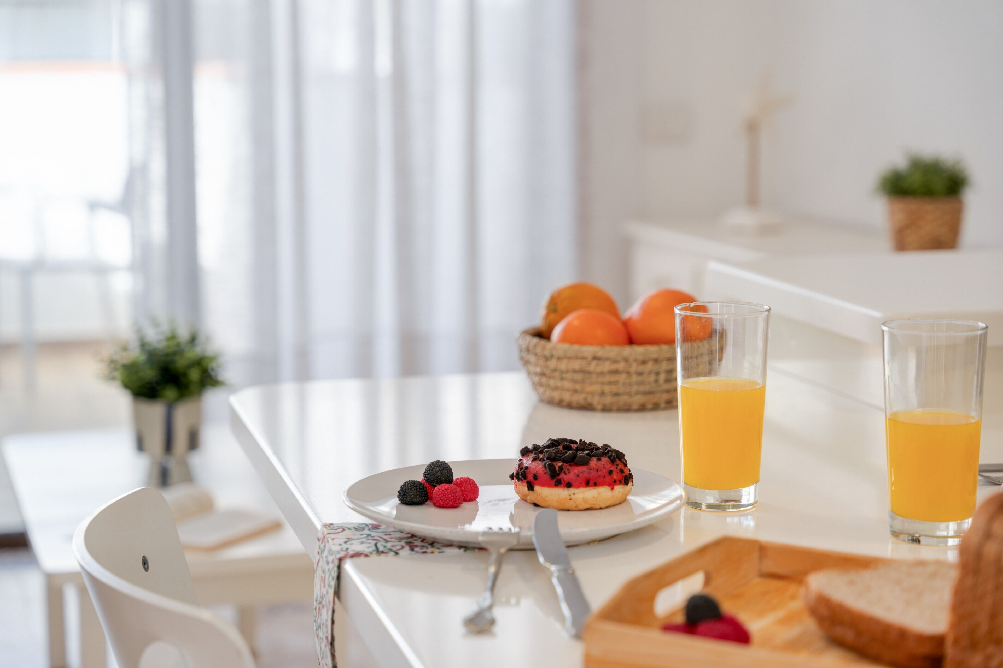 A breakfast table with a plate of berries, a donut, and two glasses of orange juice.