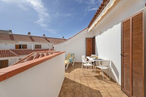 Une terrasse sur le toit, avec une table et des chaises, un transat et une vue sur les bâtiments voisins.