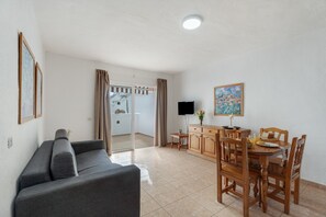 A living room with a sofa, a dining table with chairs, a TV, and a painting on the wall. - Sun and Calm Las Floritas with Shared Pool, Private Terrace and Wi-Fi (Playa de las Américas)