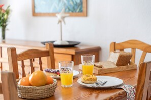 Ein Esstisch mit Frühstücksangebot, darunter eine Korb mit Orangen, zwei Gläser Orangensaft, ein Teller mit Gebäck und eine Schale mit Brot.