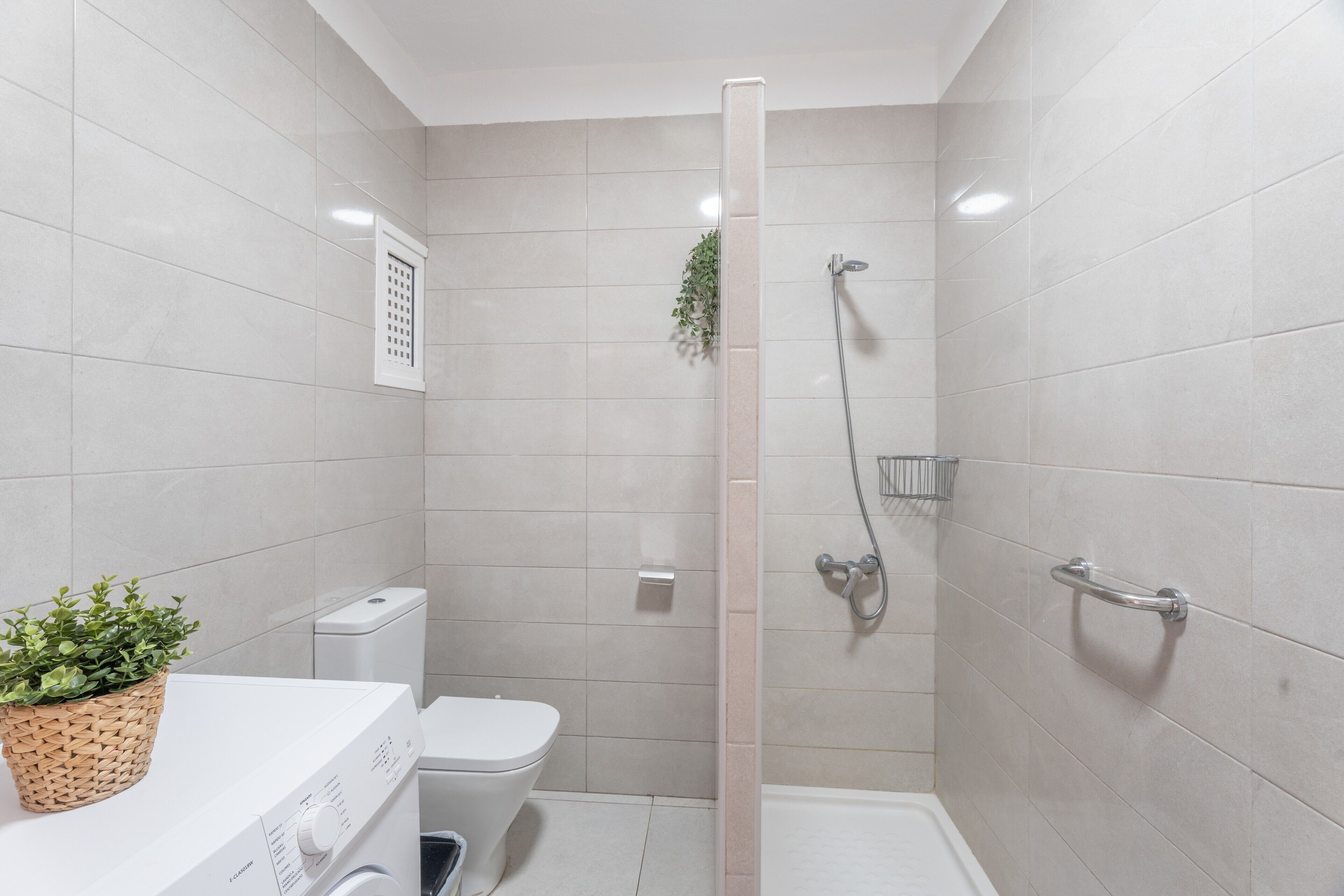 A bathroom with a shower, toilet, and washing machine.