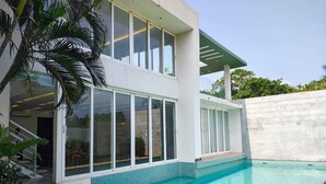 A modern house with a swimming pool, large windows, and a covered patio area. - Truliv Villa Nivara (Tirupporur)