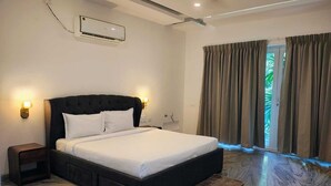 A bedroom with a large bed, a nightstand, an air conditioning unit, and a view of greenery through the curtains. - Truliv Villa Nivara (Tirupporur)