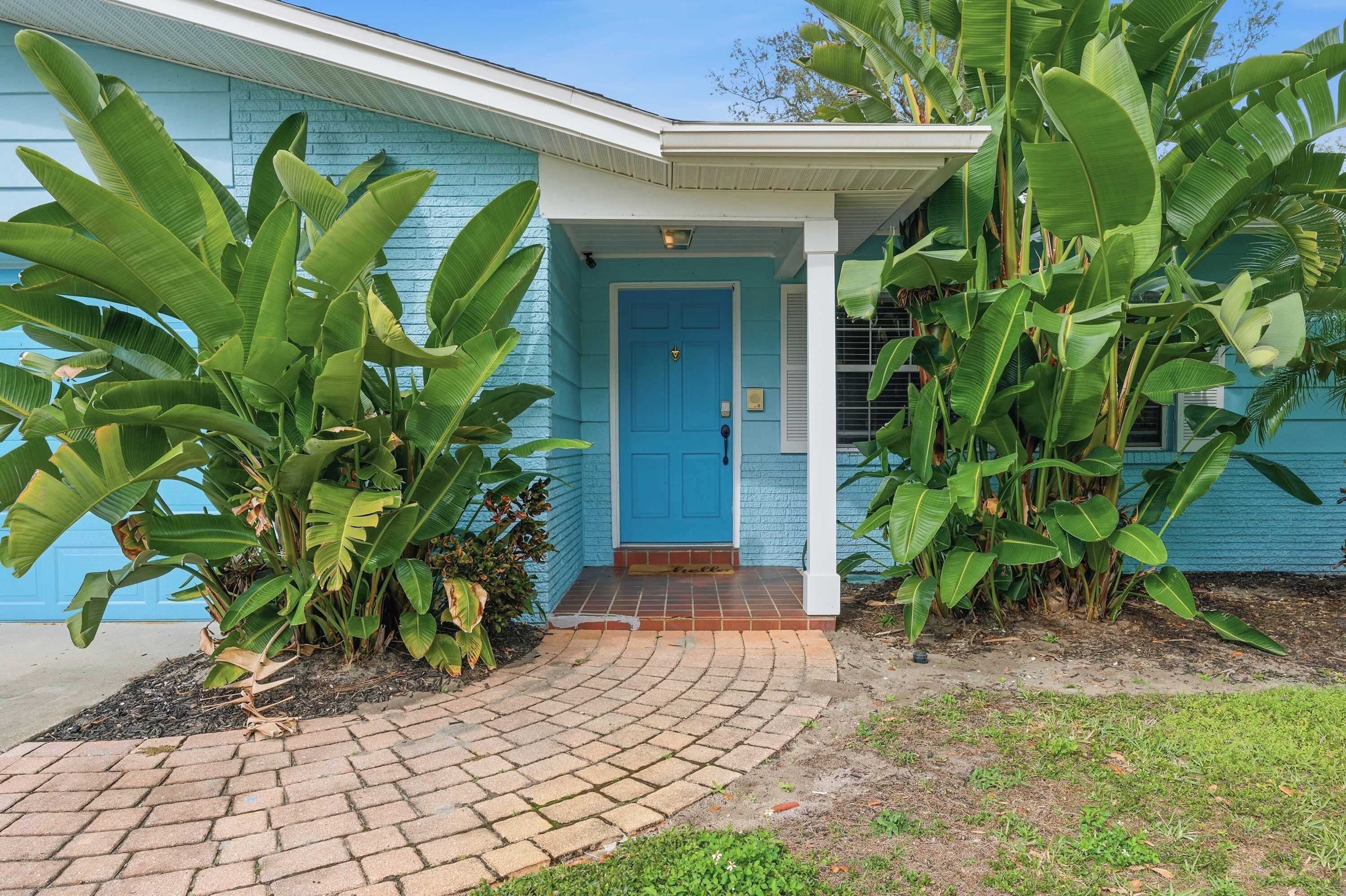Een blauw huis met een voordeur, omringd door grote bananenplanten.