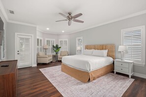 Une chambre avec un grand lit, un ventilateur de plafond, des murs blancs et un plancher en bois.