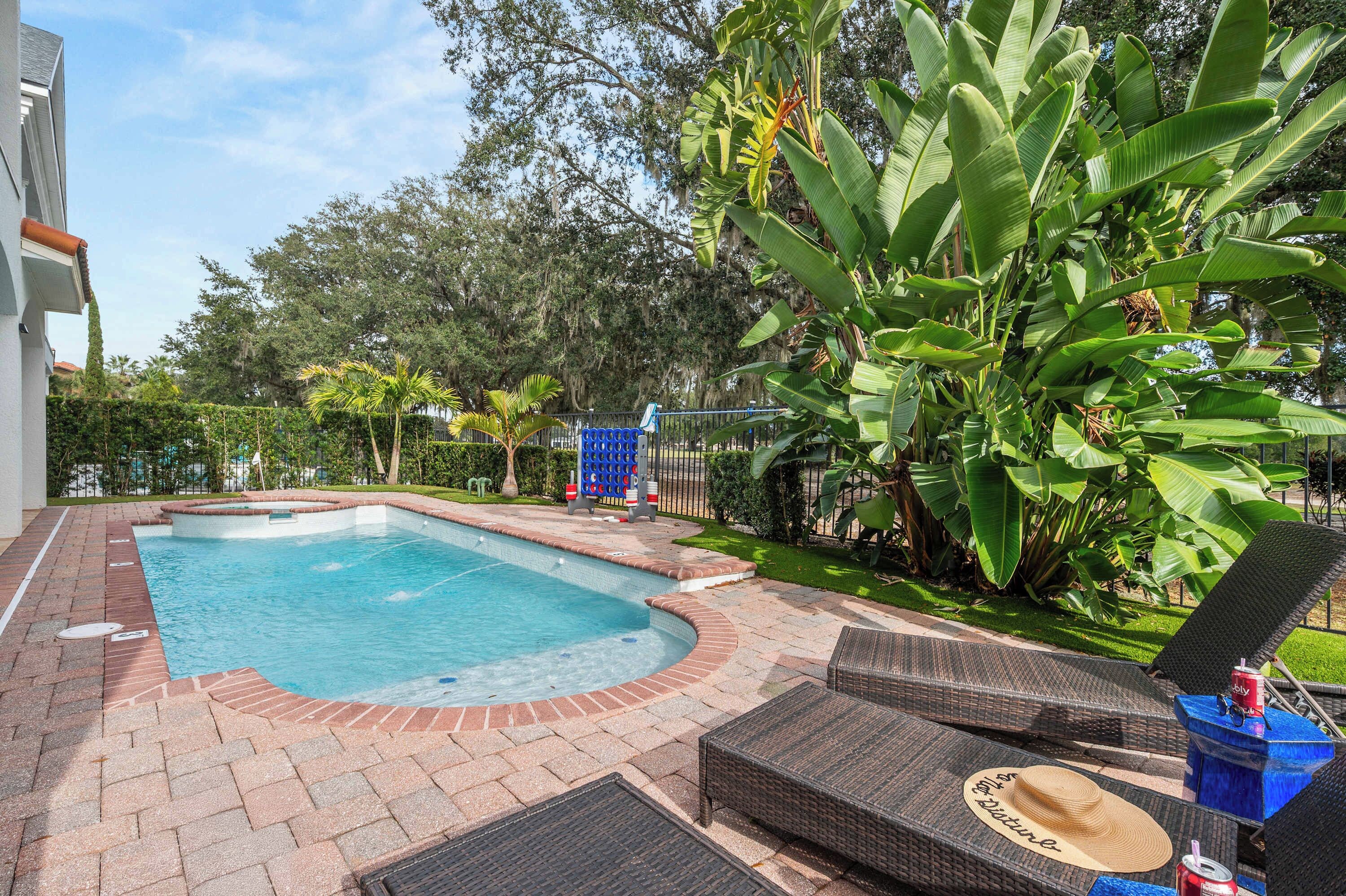 A swimming pool with a brick border, surrounded by lush greenery and a fence.