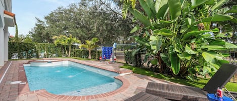 Una piscina con borde de ladrillo, rodeada de abundante vegetación y una valla.