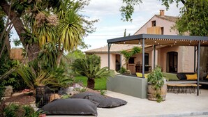 Zona de piscina con un área de estar cubierta, una palmera y una casa al fondo.