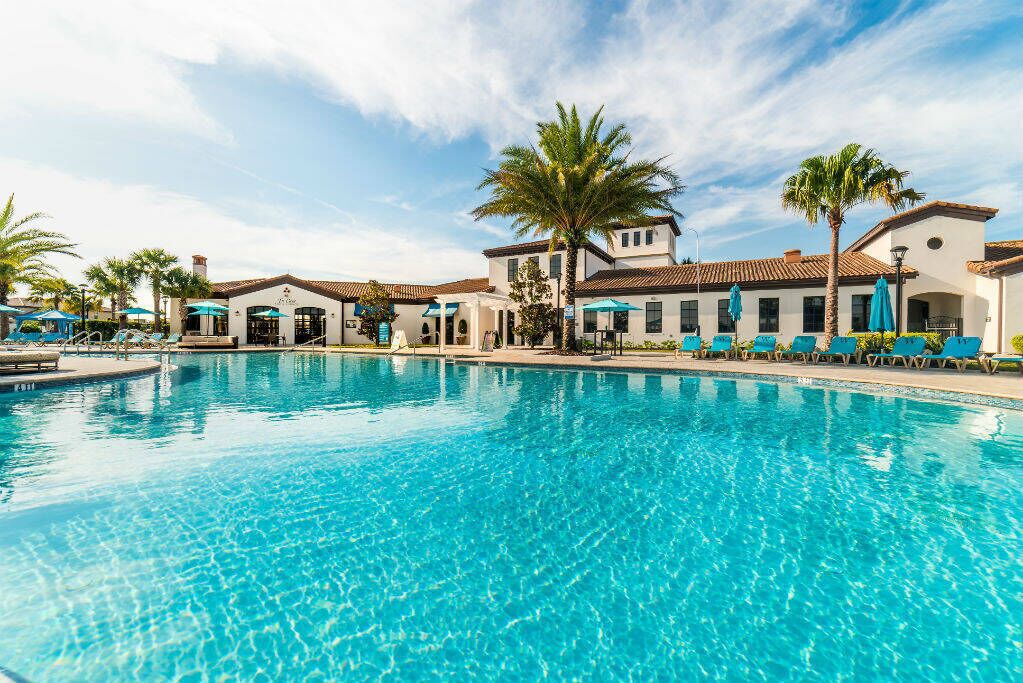 Ein Swimmingpool mit Liegestühlen und Sonnenschirmen, umgeben von Gebäuden im mediterranen Stil.