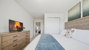 Ein Schlafzimmer mit einem Bett, einer Holzkredenz, einem Fernseher, der ein Feuer zeigt, und einer Tür zu einem anderen Raum.