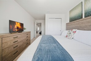 Ein Schlafzimmer mit einem Bett, einer Holzkredenz, einem Fernseher, der ein Feuer zeigt, und einer Tür zu einem anderen Raum.