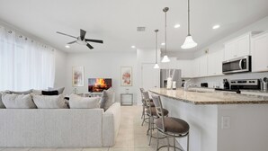 Eine moderne Küche mit weißen Schränken, einer zentralen Kochinsel mit Barhocker sowie Deckenventilator und Einbaustrahlern.
