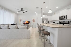 Eine moderne Küche mit weißen Schränken, einer zentralen Kochinsel mit Barhocker sowie Deckenventilator und Einbaustrahlern.
