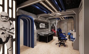 Ein Star Wars-zimmer mit Spieltisch, blauen Gaming-Stühlen und einer Darth-Vader-Statue.