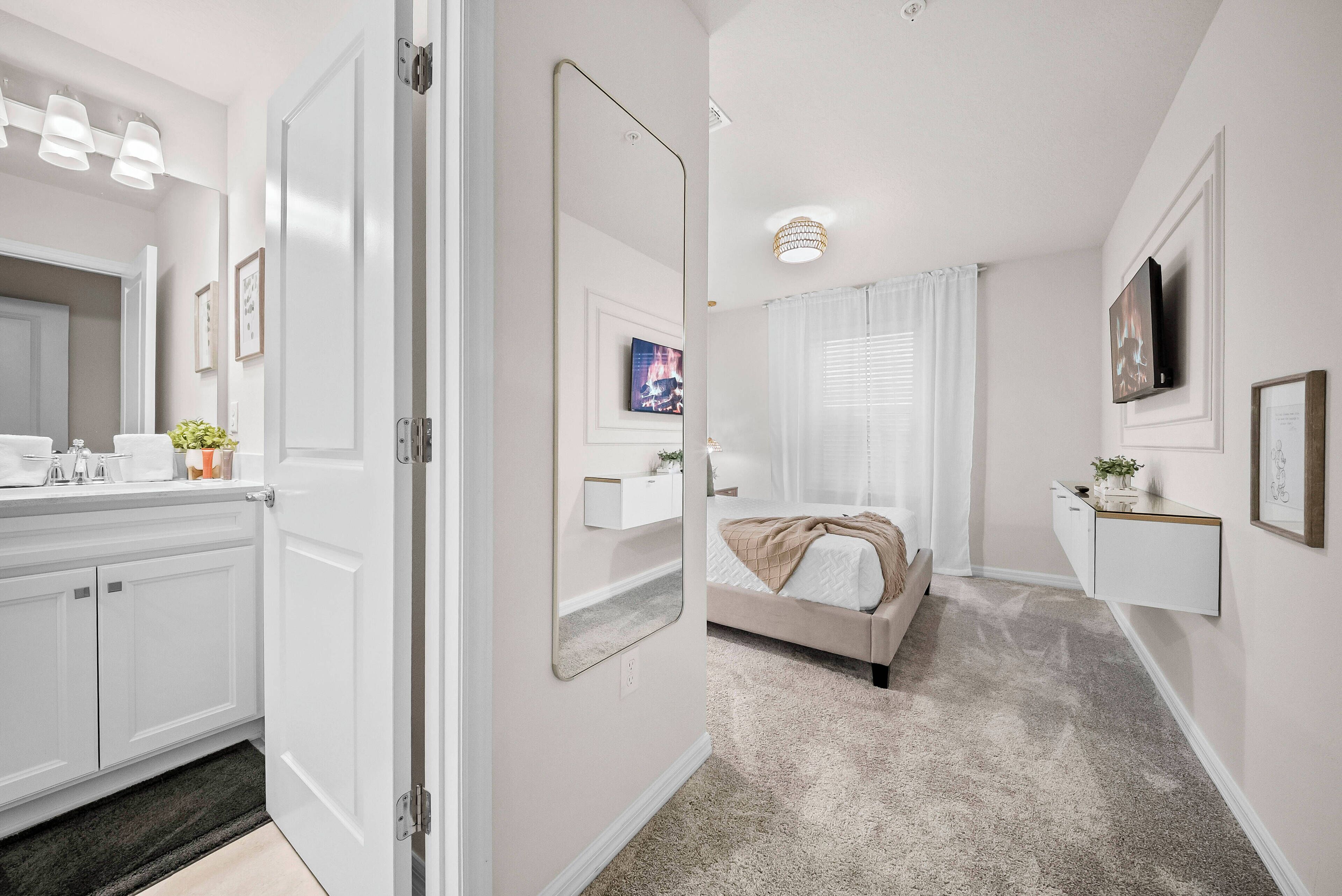 Experience a beautifully designed space with soft gray carpeting and a bright atmosphere. Unwind in a stylish bathroom with modern fixtures and a large mirror, while the cozy bedroom features inviting bedding and tasteful decor.