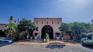 A building with an arched entrance, surrounded by potted plants and a gravel driveway. - Escale Nature near Marrakech | Private Bungalows, Pool, Terrace & Hammam (Marrakech)