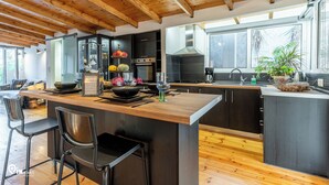 Eine moderne Küche mit Holzbalken, einer zentralen Kochinsel, Barhocker und einem großen Fenster.