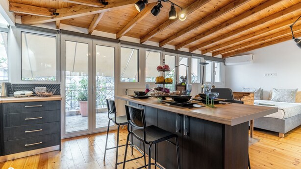 Eine moderne Küche mit Holzboden, großen Fenstern und einer zentralen Kochinsel mit Barhocker.
