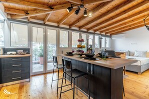 A modern kitchen with a wooden ceiling, large windows, and a central island with bar stools. - Rustic - Private Rooftop Garden & City View Athens (Egaleo)