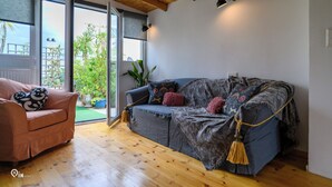 Ein gemütliches Wohnzimmer mit Holzboden, einer Couch, einem Sessel und einem großen Fenster mit Blick auf Grünflächen.