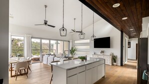 A spacious kitchen with a large island, wooden flooring, and pendant lighting. - Modern Hill Country Home ~ Sunset Views and BBQ (Austin)
