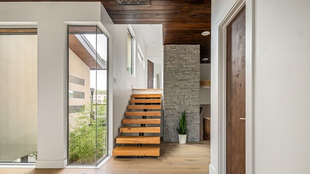 A modern interior with a wooden staircase, a stone wall, and a glass door leading to an outdoor area. - Modern Hill Country Home ~ Sunset Views and BBQ (Austin)