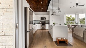 A modern kitchen with stainless steel appliances, a wooden ceiling, and a dining area with a view. - Modern Hill Country Home ~ Sunset Views and BBQ (Austin)